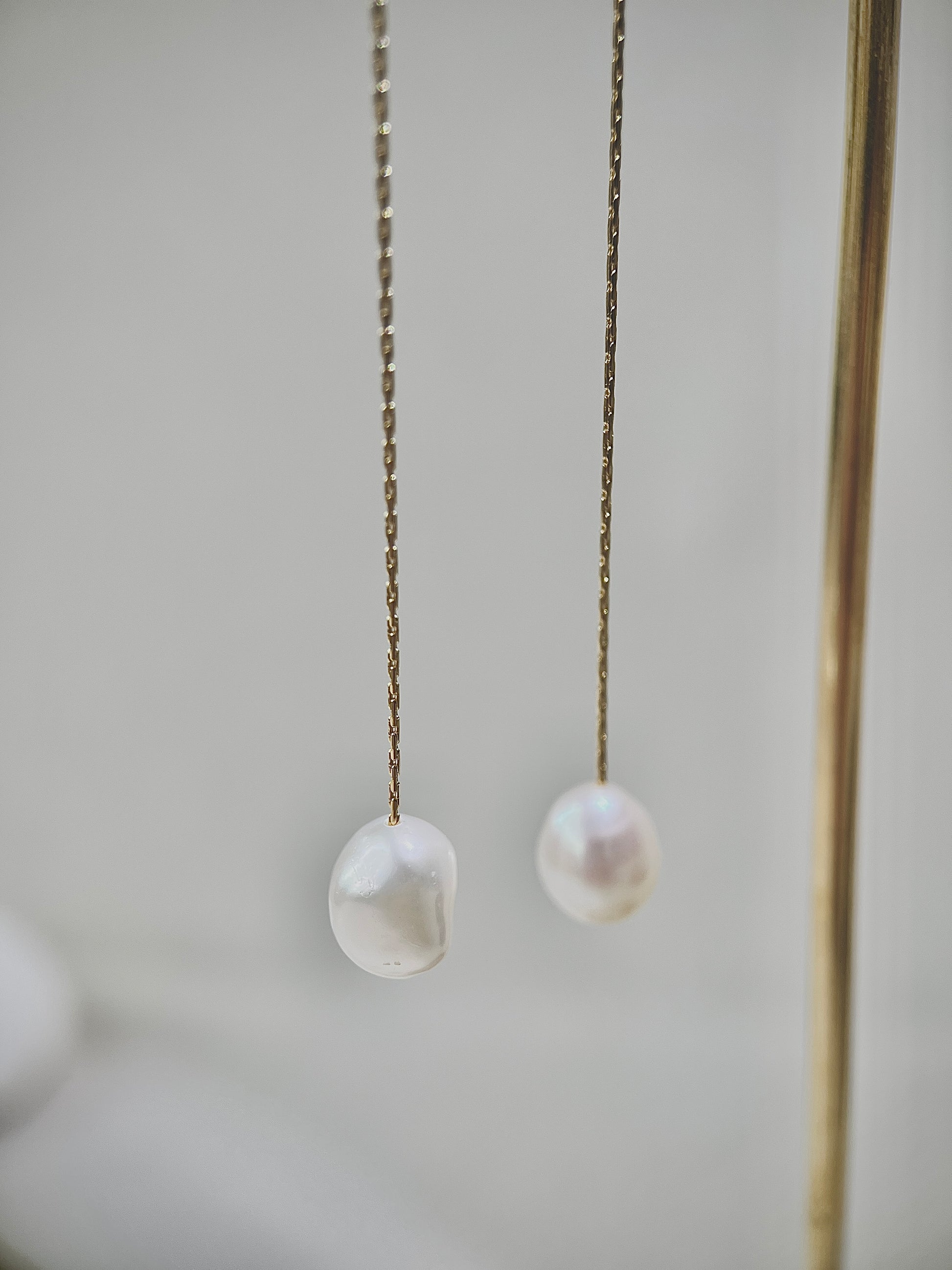 Two pearl earrings hanging on a chain against a neutral background