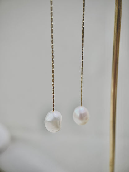 Two pearl earrings hanging on a chain against a neutral background