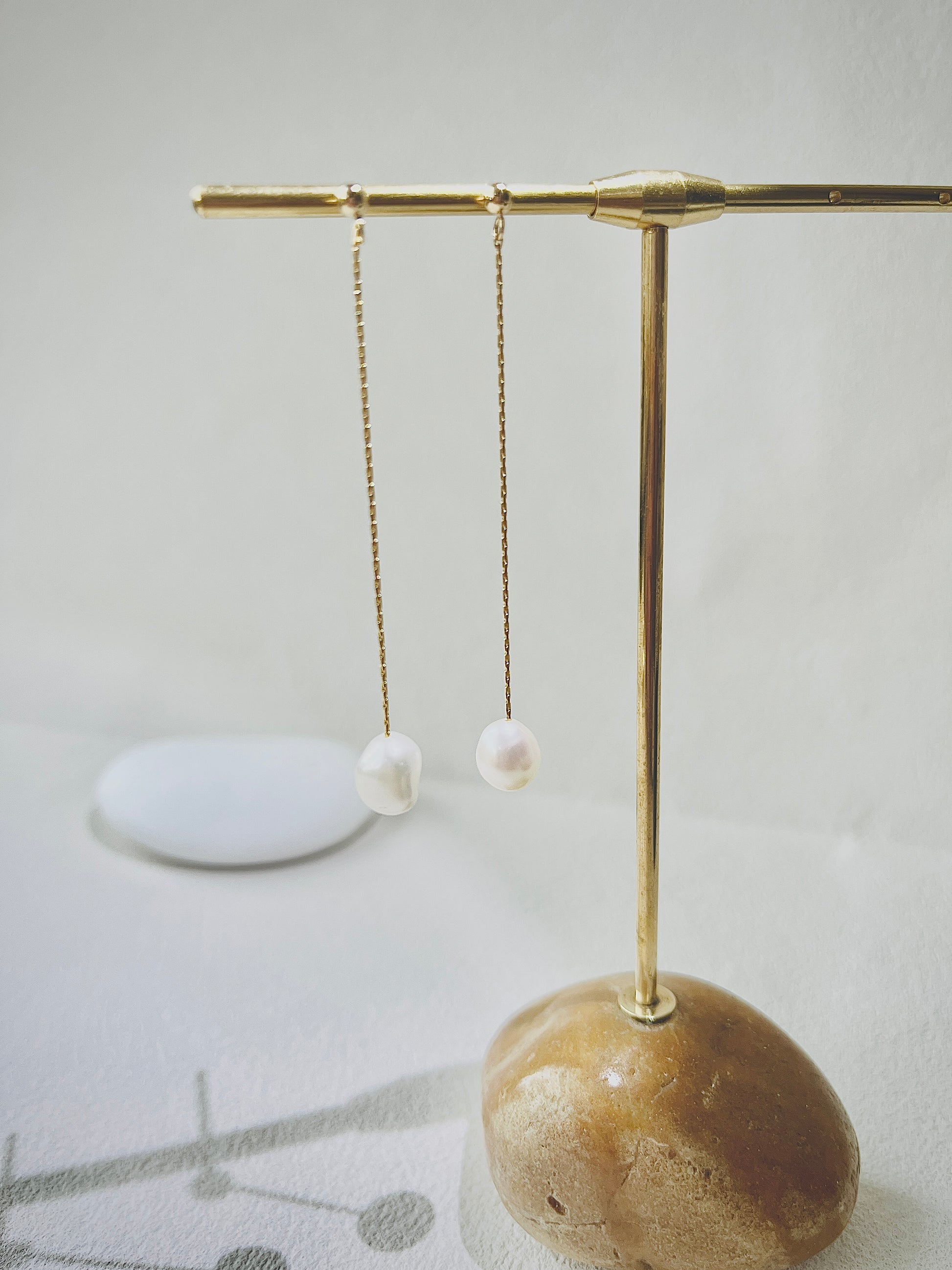 Pearl earrings on a gold stand with a stone base against a light background
