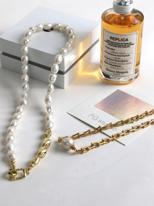 Pearl necklace for men and gold chain on a white surface with a bottle labeled 'Replica' and a book.