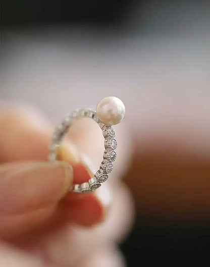Close-up of a ring with a pearl and diamonds held between fingers against a blurred background