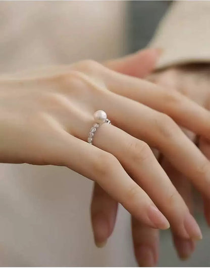 Close-up of a hand wearing a silver ring with a pearl on a neutral background