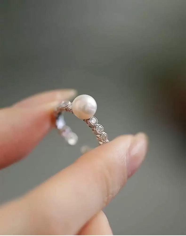 Silver ring with a pearl held between fingers against a blurred background