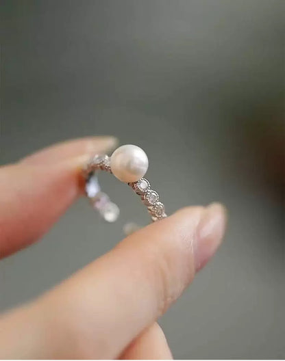 Silver ring with a pearl held between fingers against a blurred background