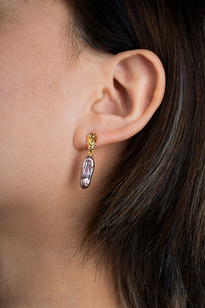 Close-up of an ear wearing a gold earring with a purple pearl.