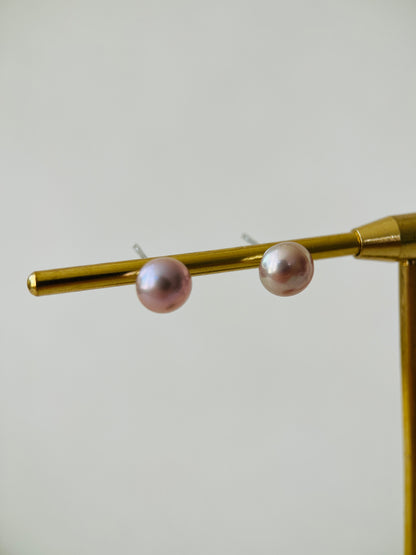 Pearl earrings on a gold stand against a light gray background
