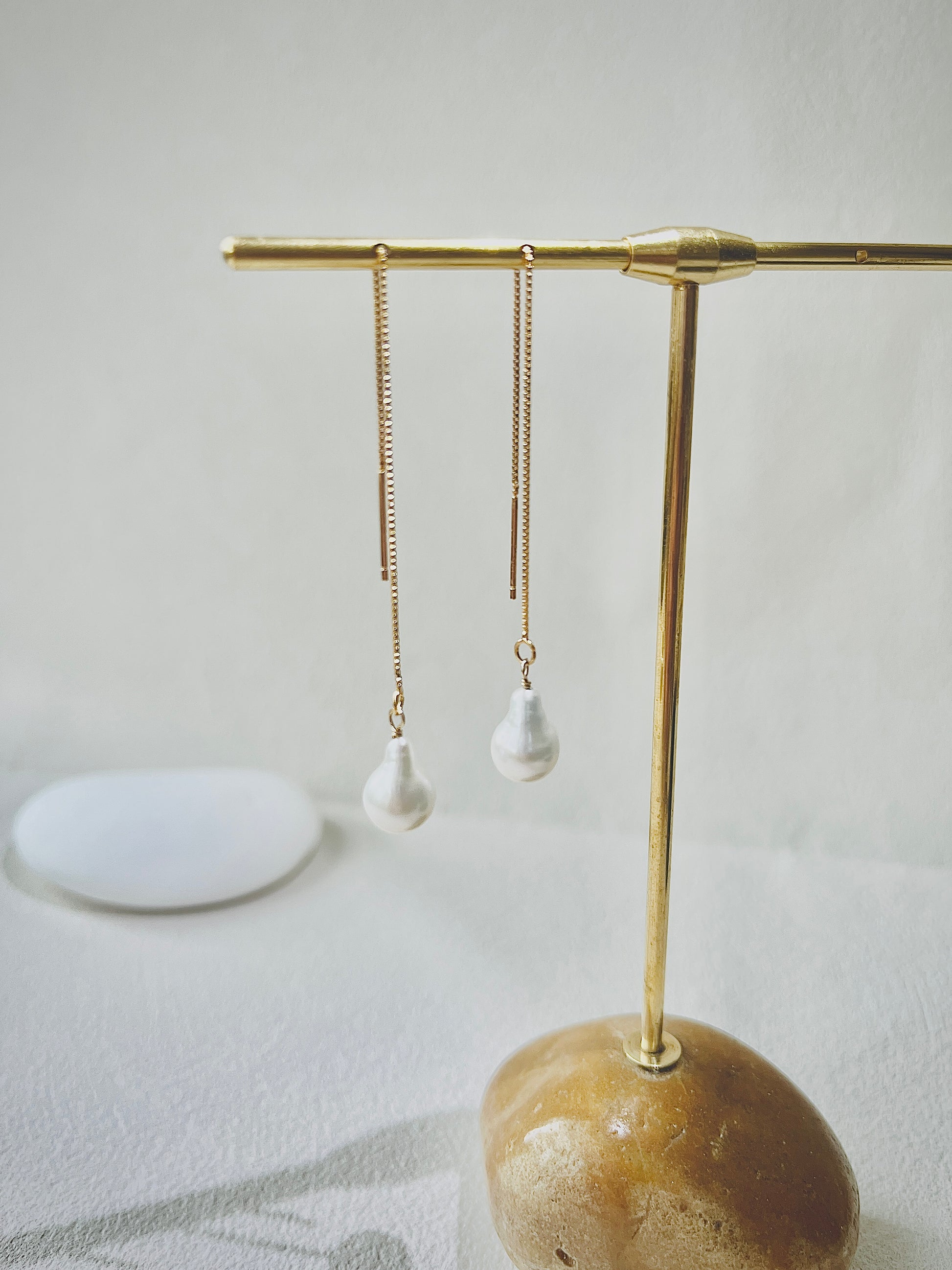 Gold earring stand with pearl earrings on a neutral background