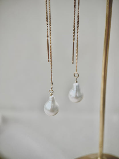 Pearl drop earrings hanging from gold chains against a neutral background