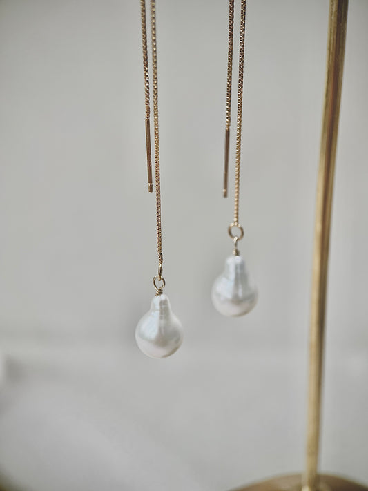Pearl drop earrings hanging from gold chains against a neutral background