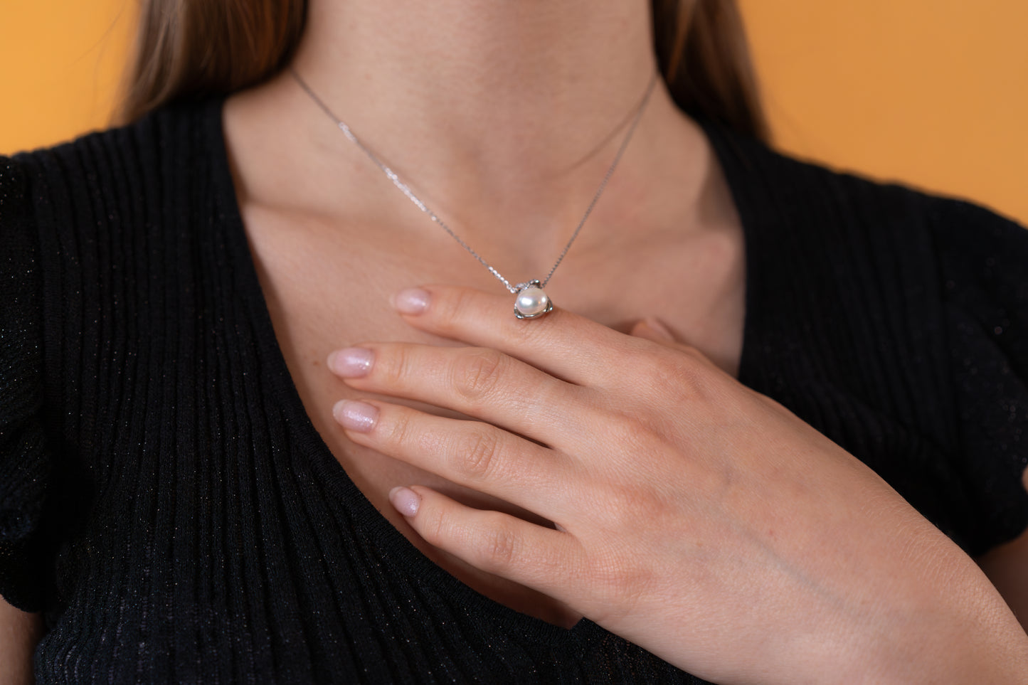 Person wearing a necklace with a pearl pendant against a yellow background