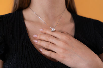 Person wearing a necklace with a pearl pendant against a yellow background