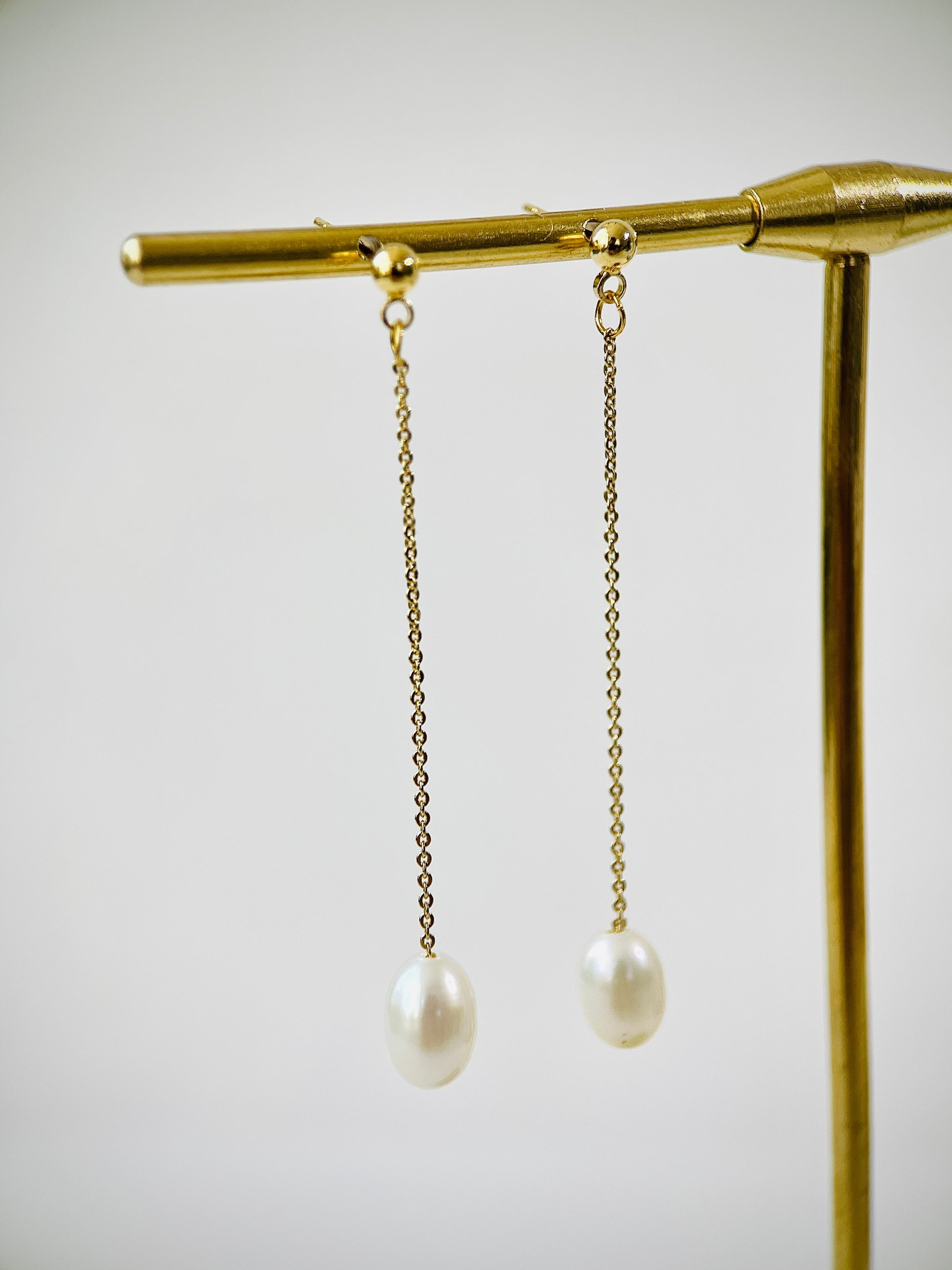 Pearl earrings hanging from a gold stand against a light background