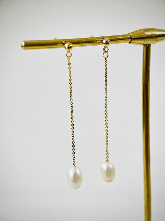 Pearl earrings hanging from a gold stand against a light background