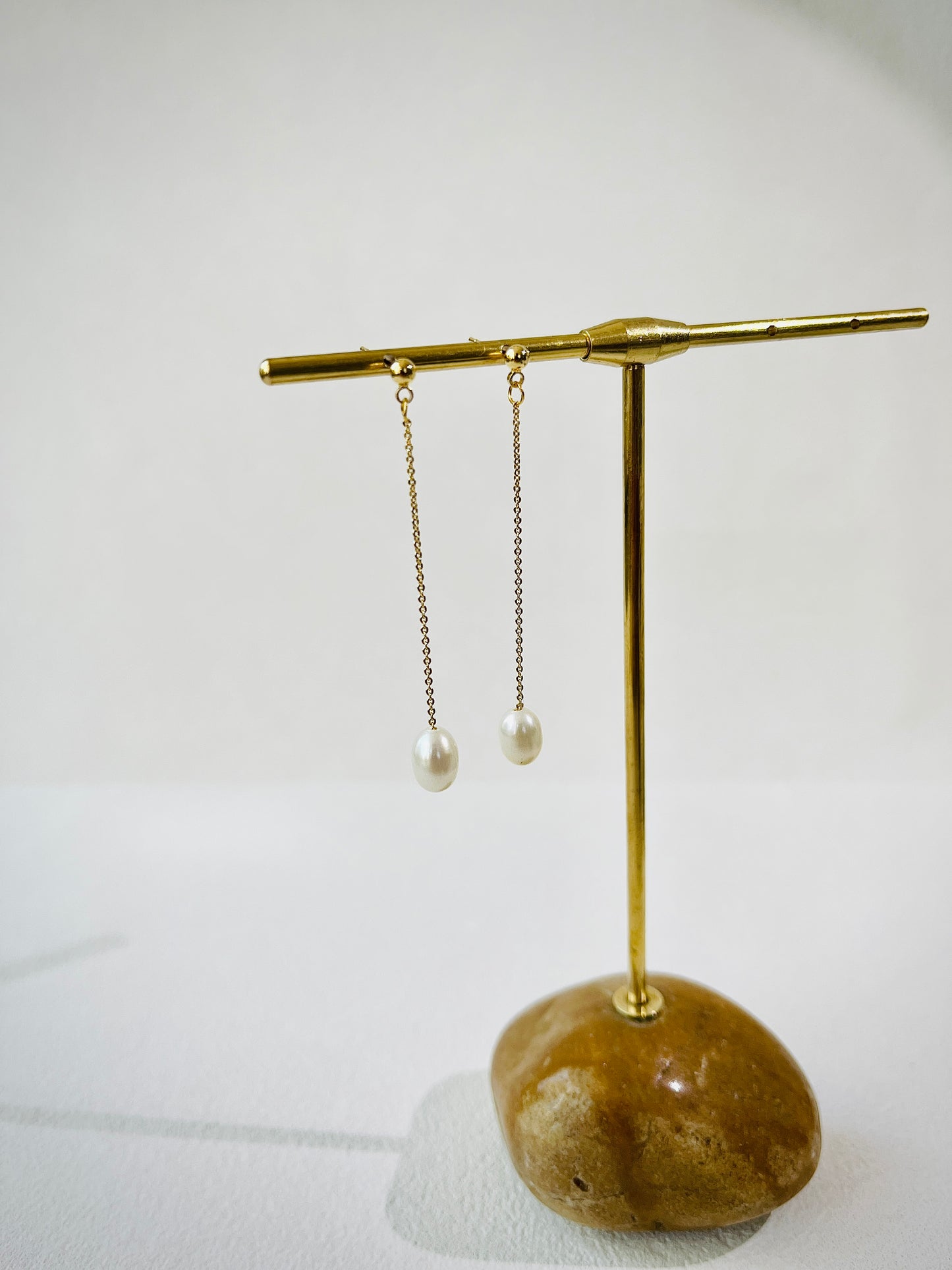 Gold earring stand with pearl earrings on a white background