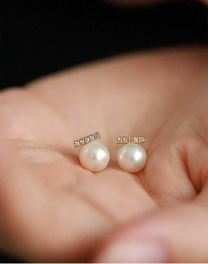Pearl earrings held in a hand with a blurred background