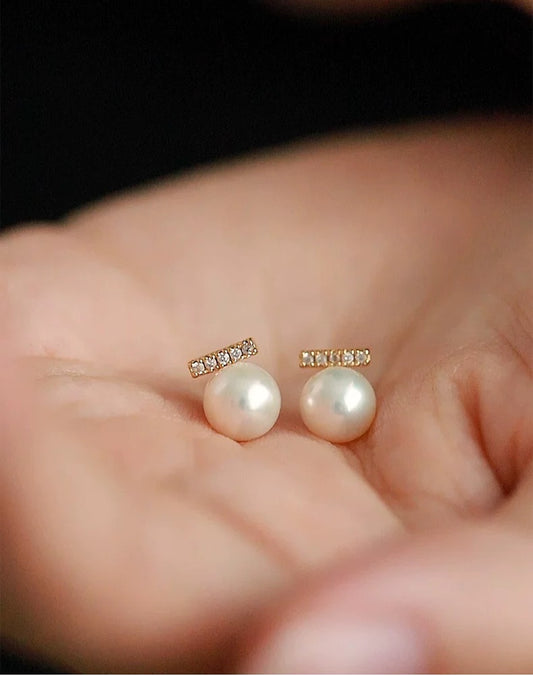 Pearl earrings held in a hand with a blurred background