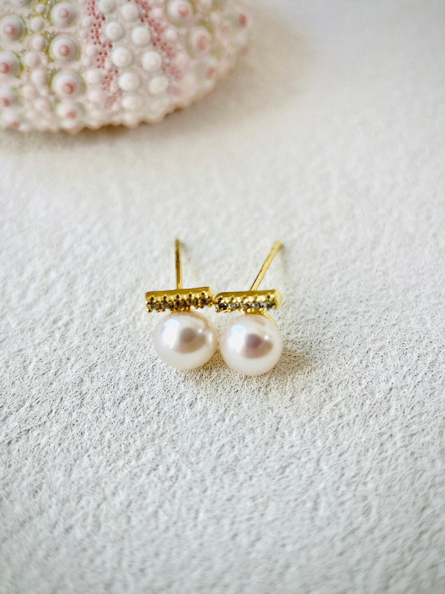 Pearl earrings with gold setting on a textured white surface