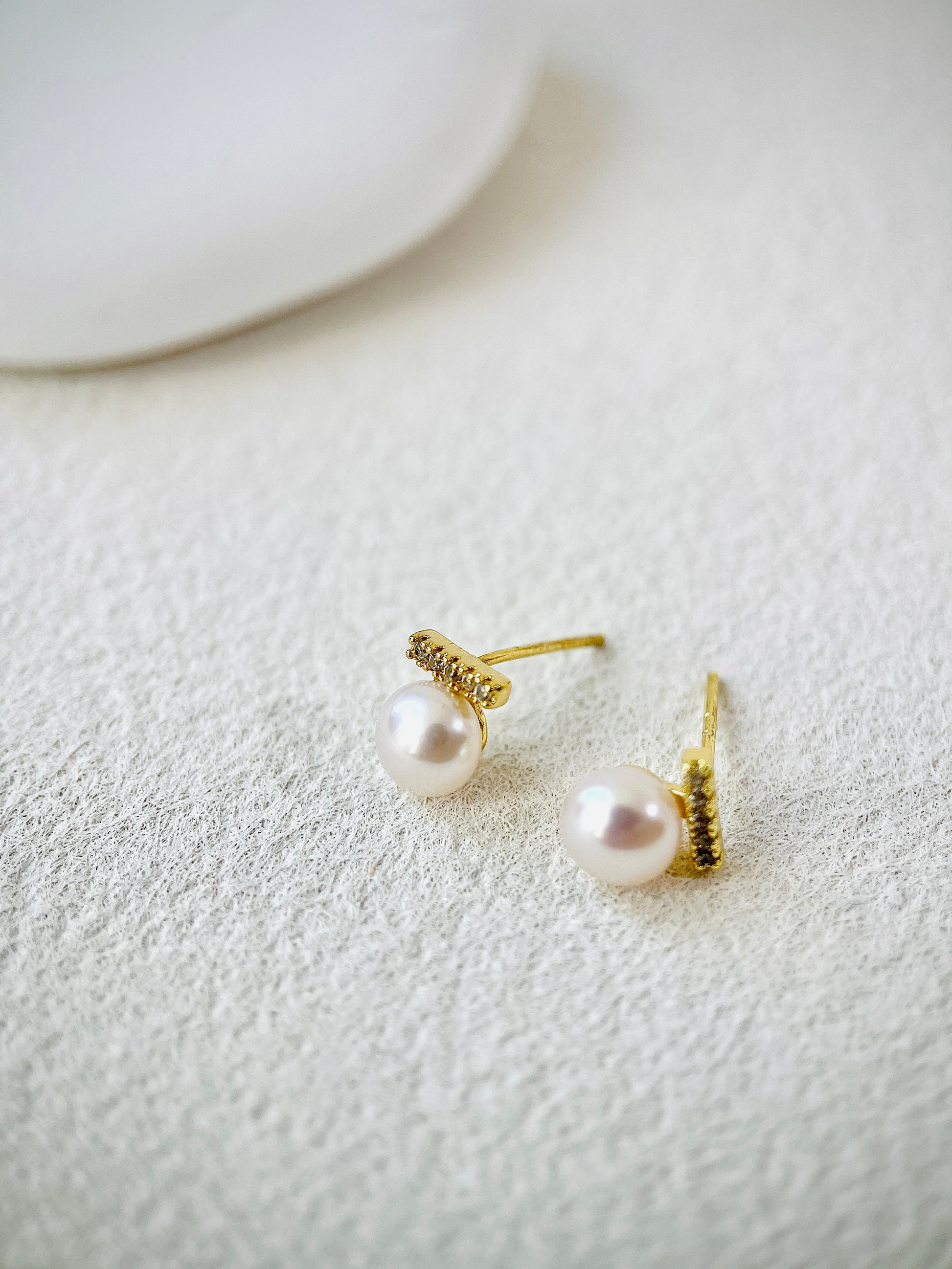 Pair of pearl earrings with gold accents on a textured white surface