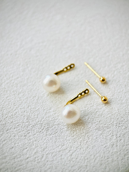 Pearl earrings with gold posts on a light gray background