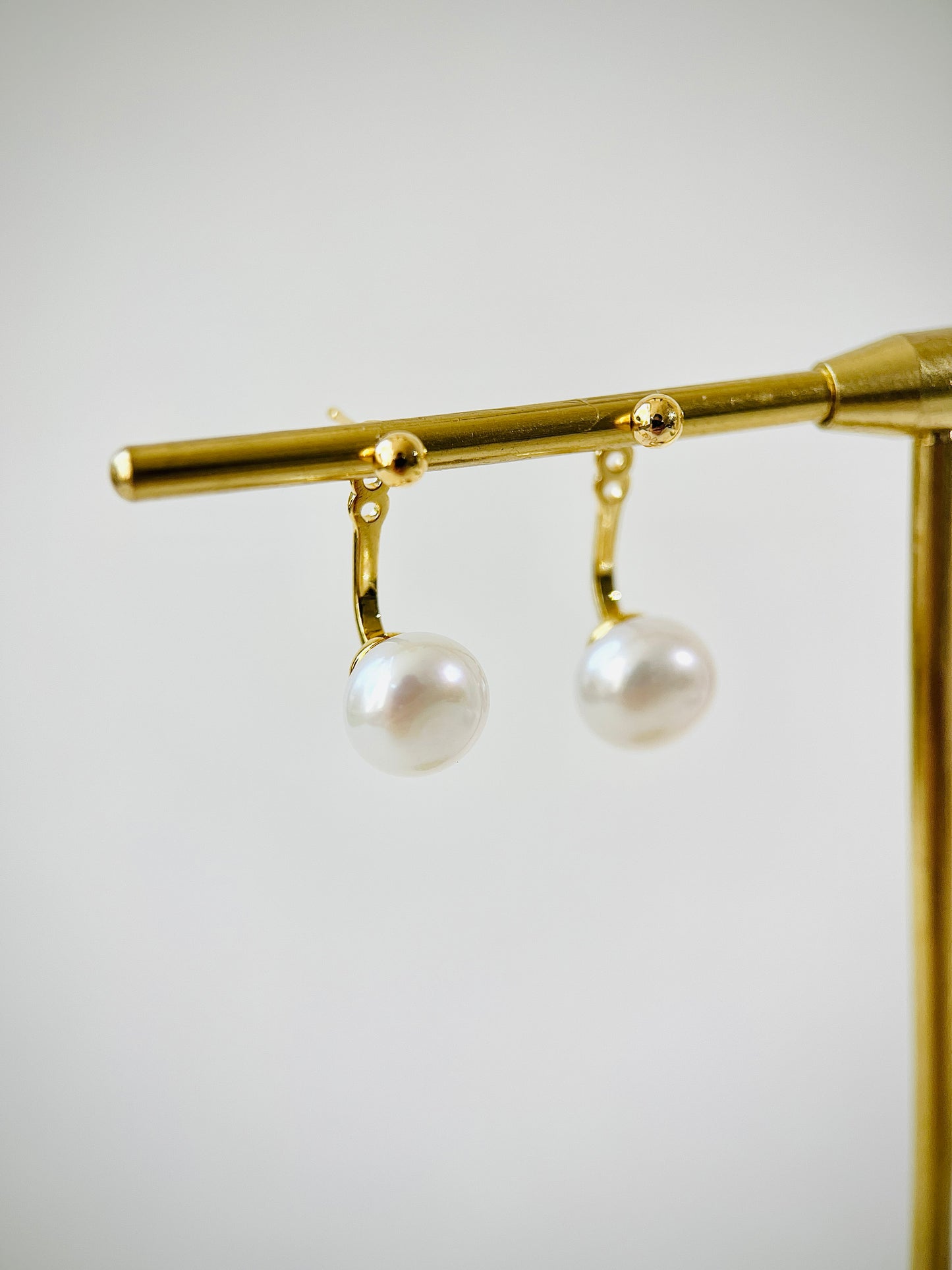 Gold earring with two pearls on a gold stand against a light gray background