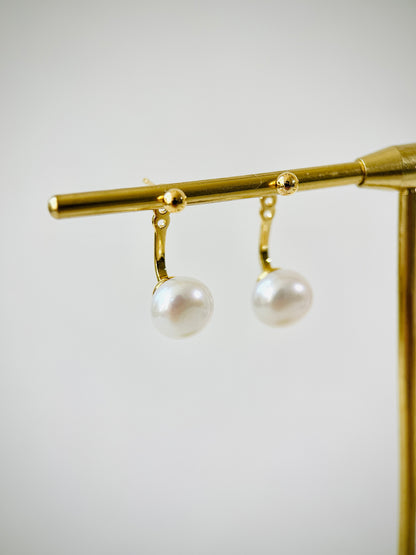 Gold earring with two pearls on a gold stand against a light gray background