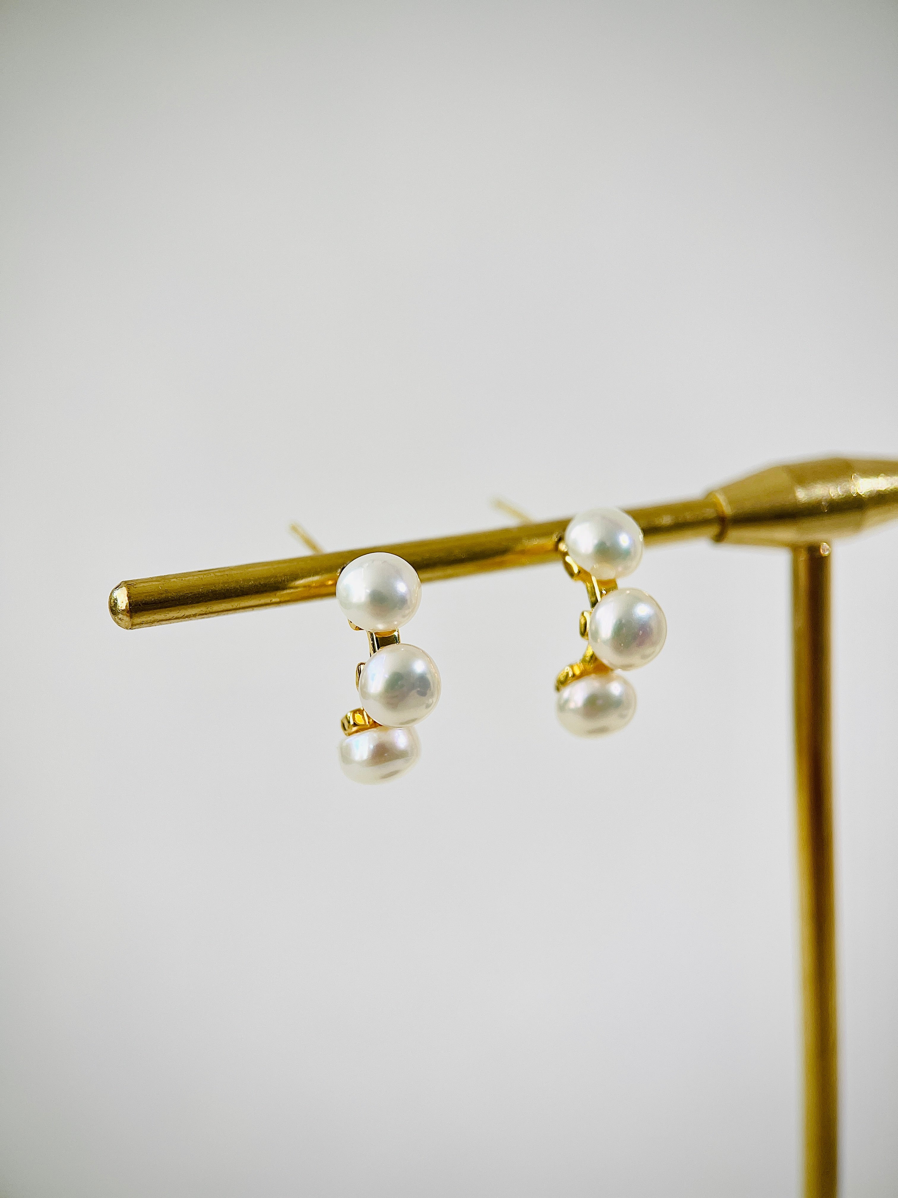 Pearl earrings on a gold stand against a light background