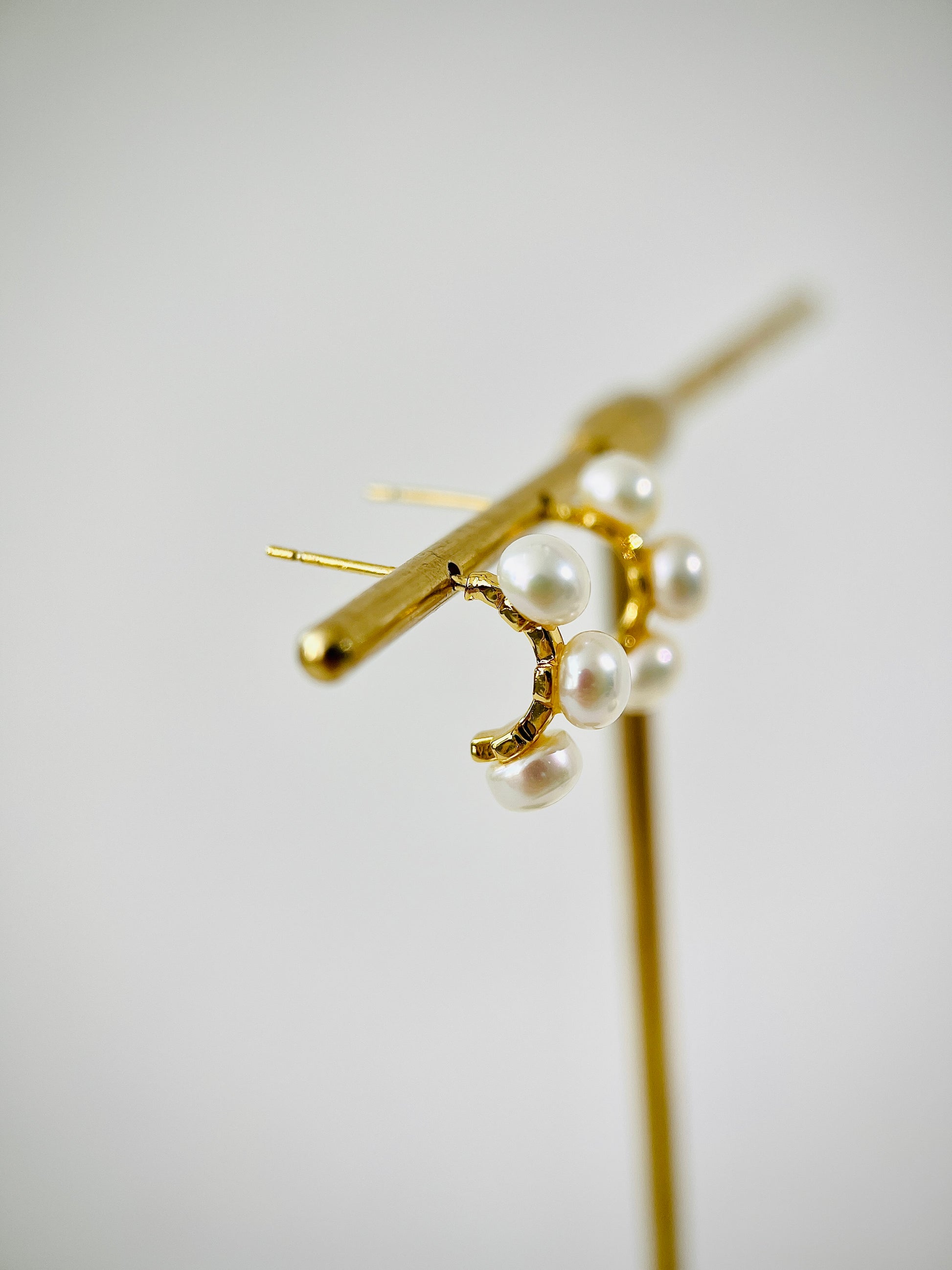 Gold earring with pearl-like beads on a light gray background