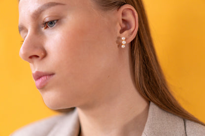 Close-up of a woman wearing white pearl climber earrings against a yellow background