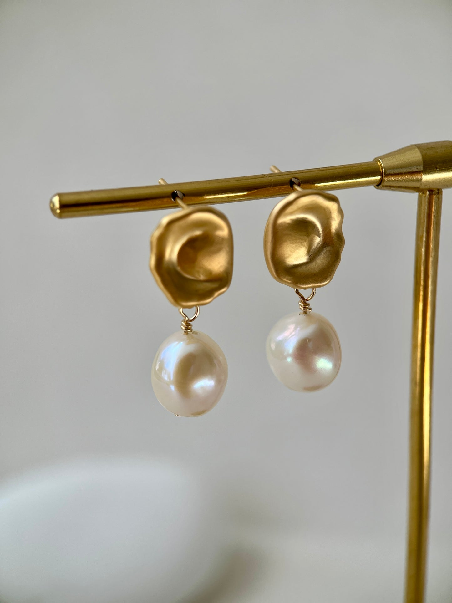 Gold earrings with pearl drops on a gold stand against a light background