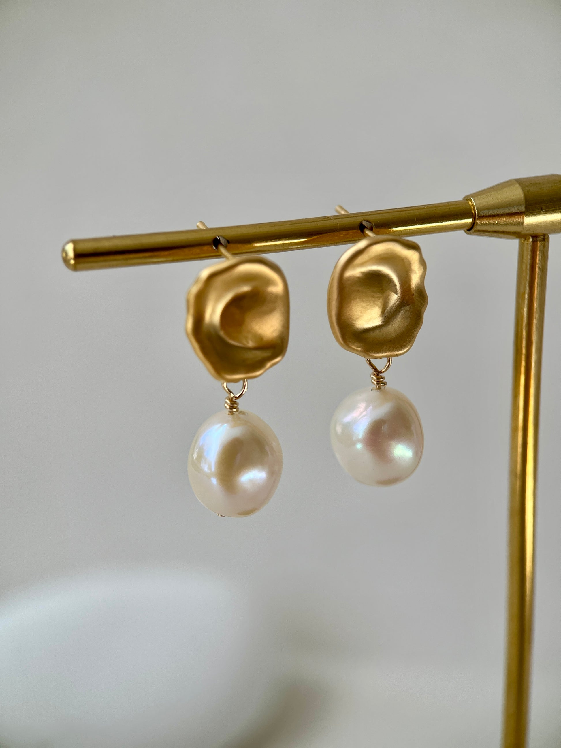 Gold earrings with pearl drops on a gold stand against a light background