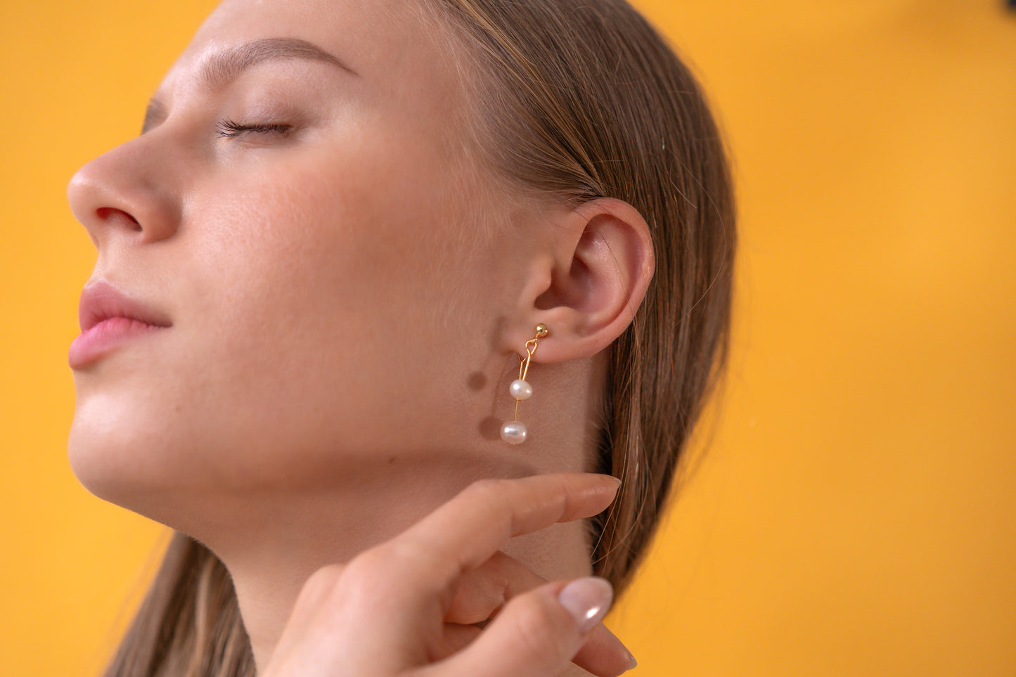 Close-up of a woman wearing golden white pearl earrings against a yellow background