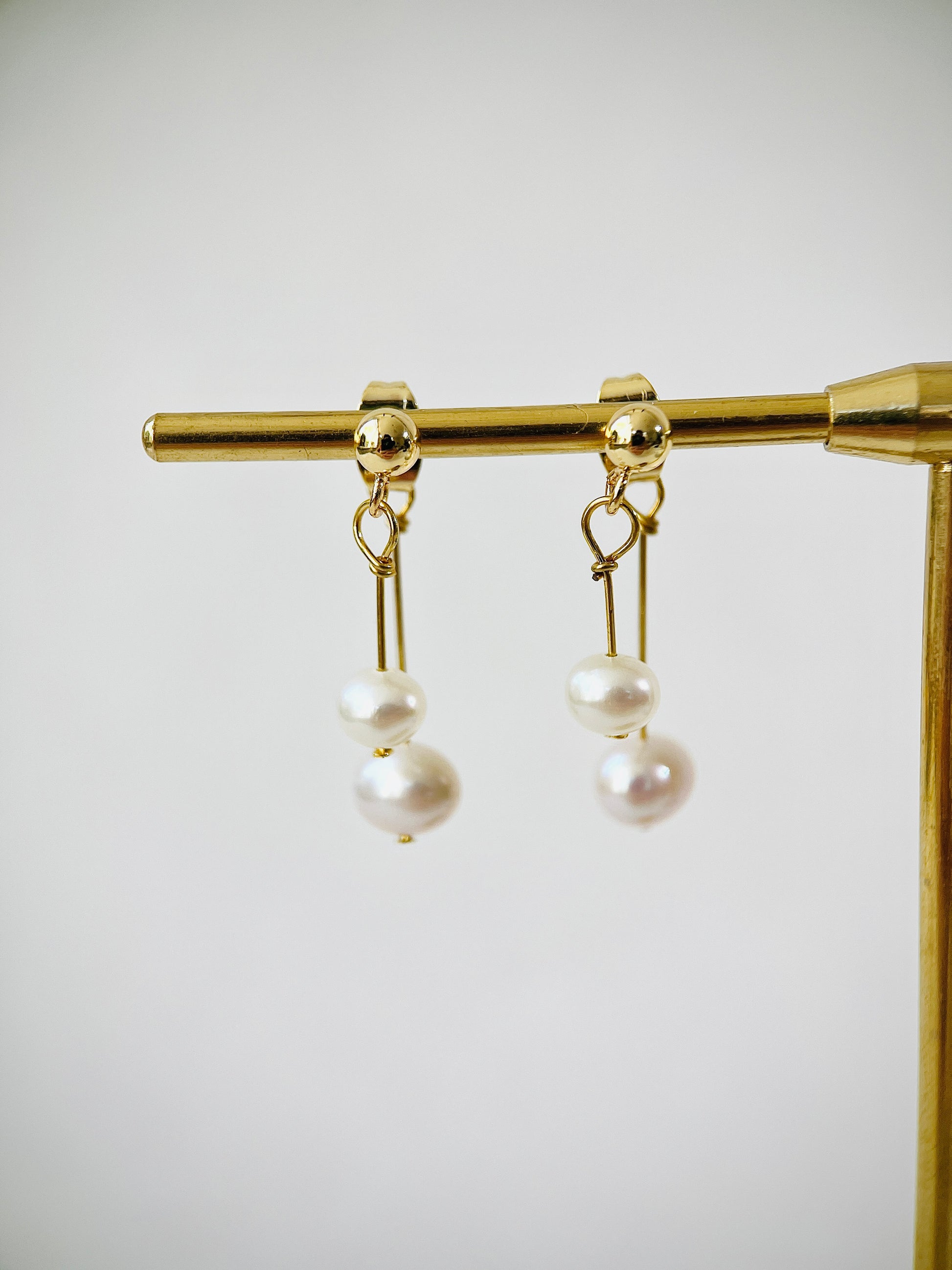 Pair of pearl earrings on a gold stand against a white background