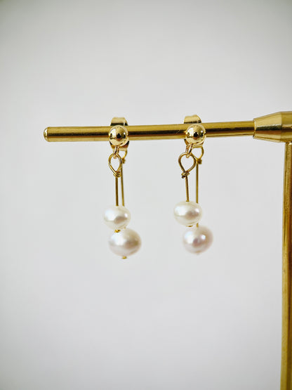 Pair of pearl earrings on a gold stand against a white background