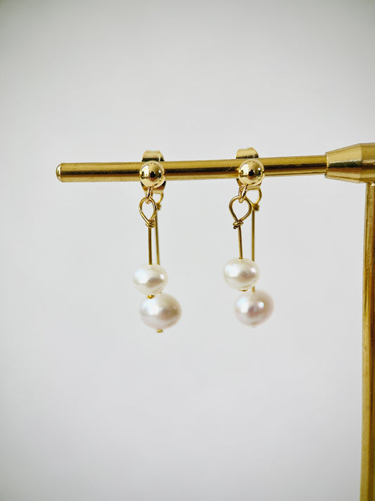 Pair of pearl earrings on a gold stand against a white background