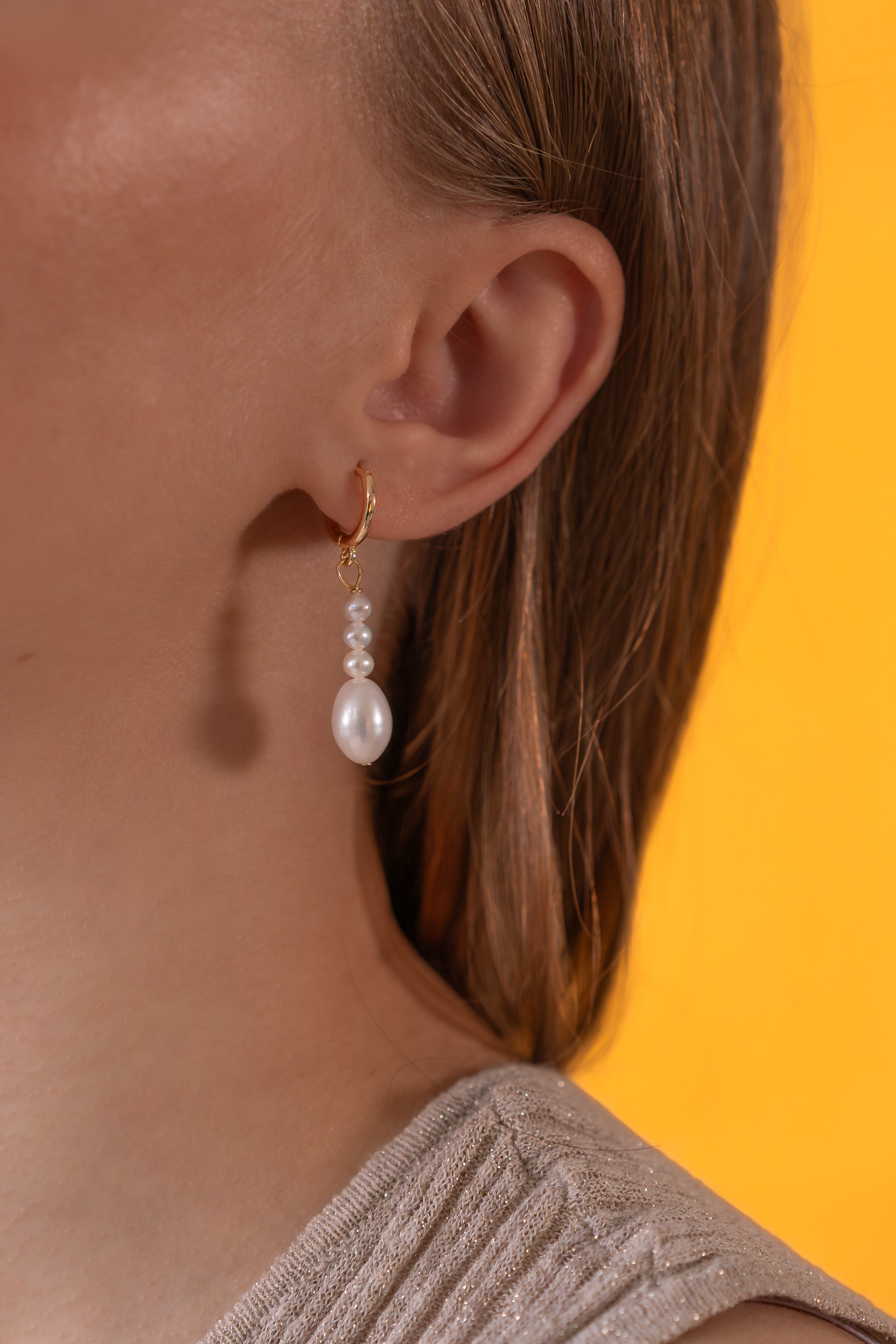 White Freshwater pearl earrings worn by a person with a yellow background