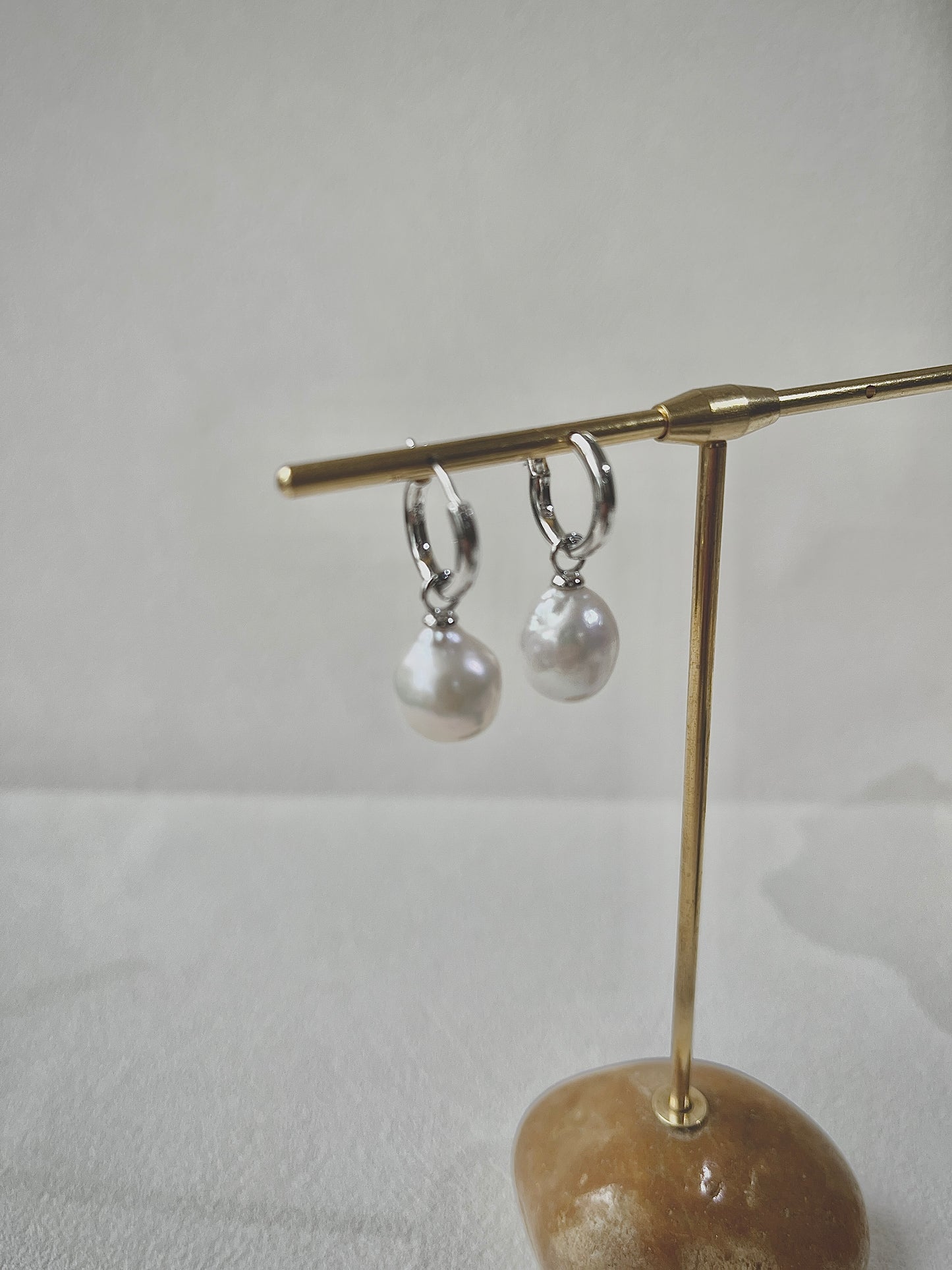 Pair of pearl earrings on a gold stand against a white background