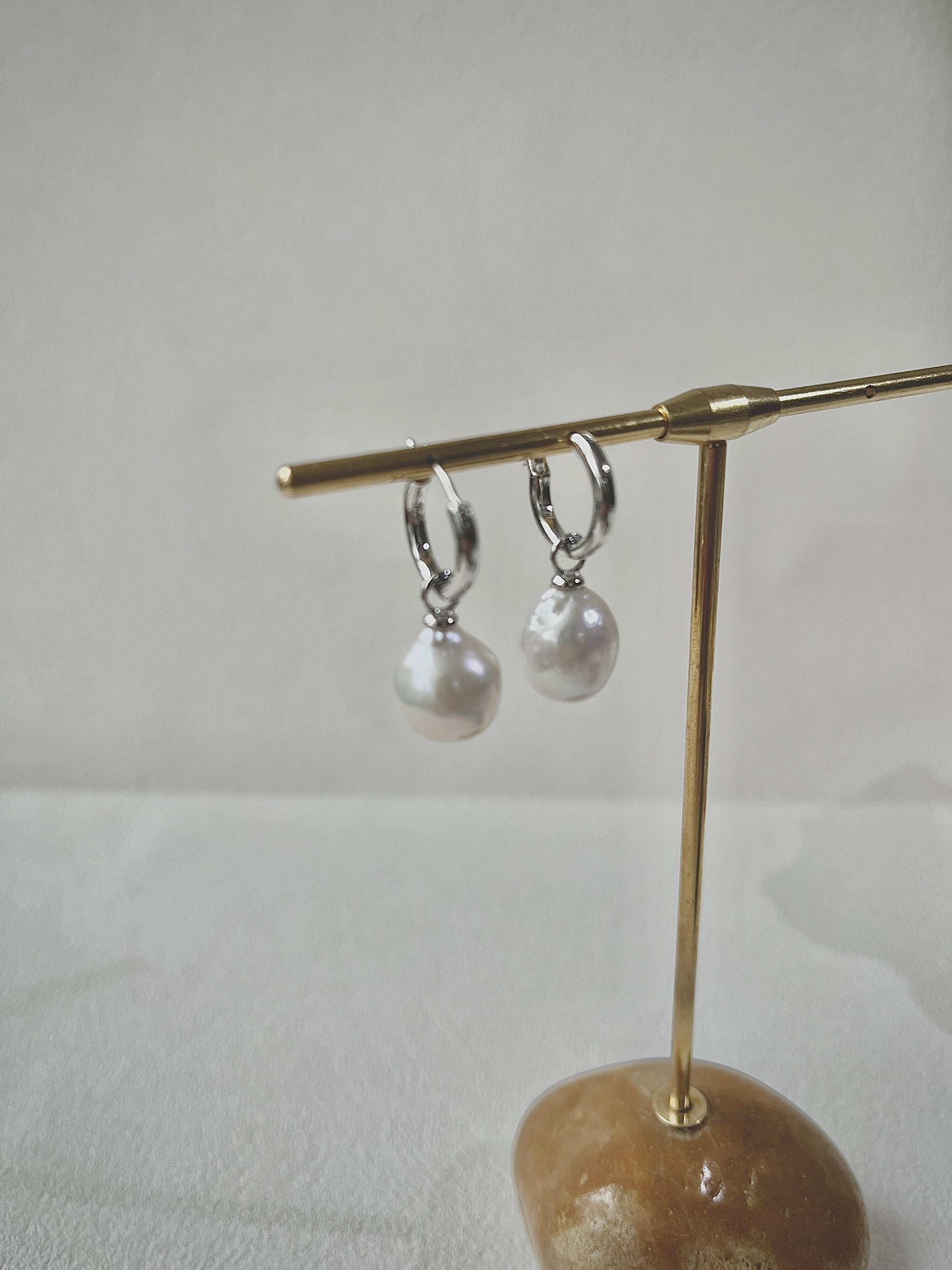 Pair of pearl earrings on a gold stand against a white background