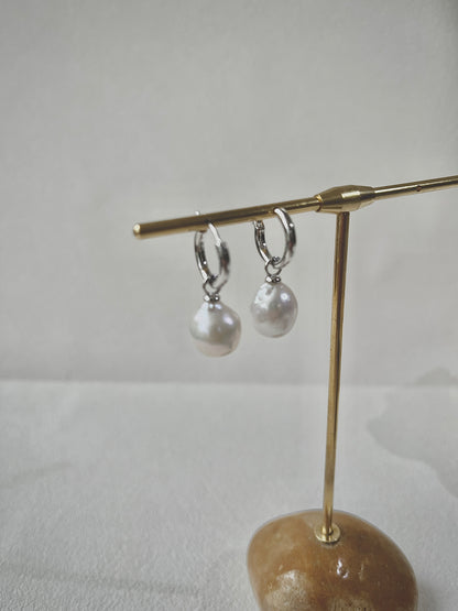 Pair of pearl earrings on a gold stand against a white background