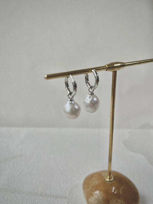 Pair of pearl earrings on a gold stand against a white background