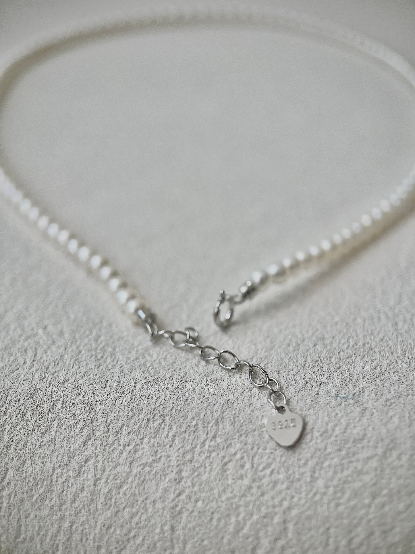 Pearl necklace with a silver clasp on a light gray background