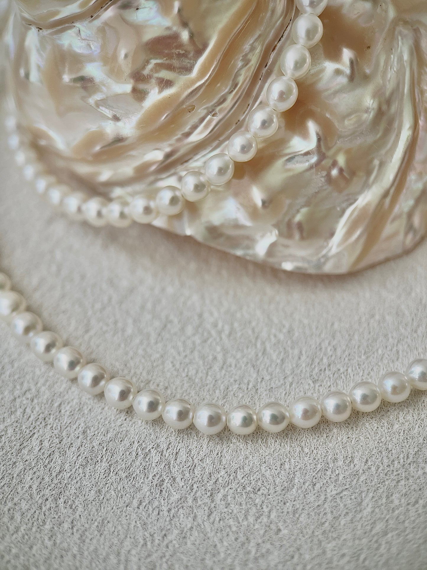 white Pearl necklace on a textured surface with a decorative glass bowl in the background
