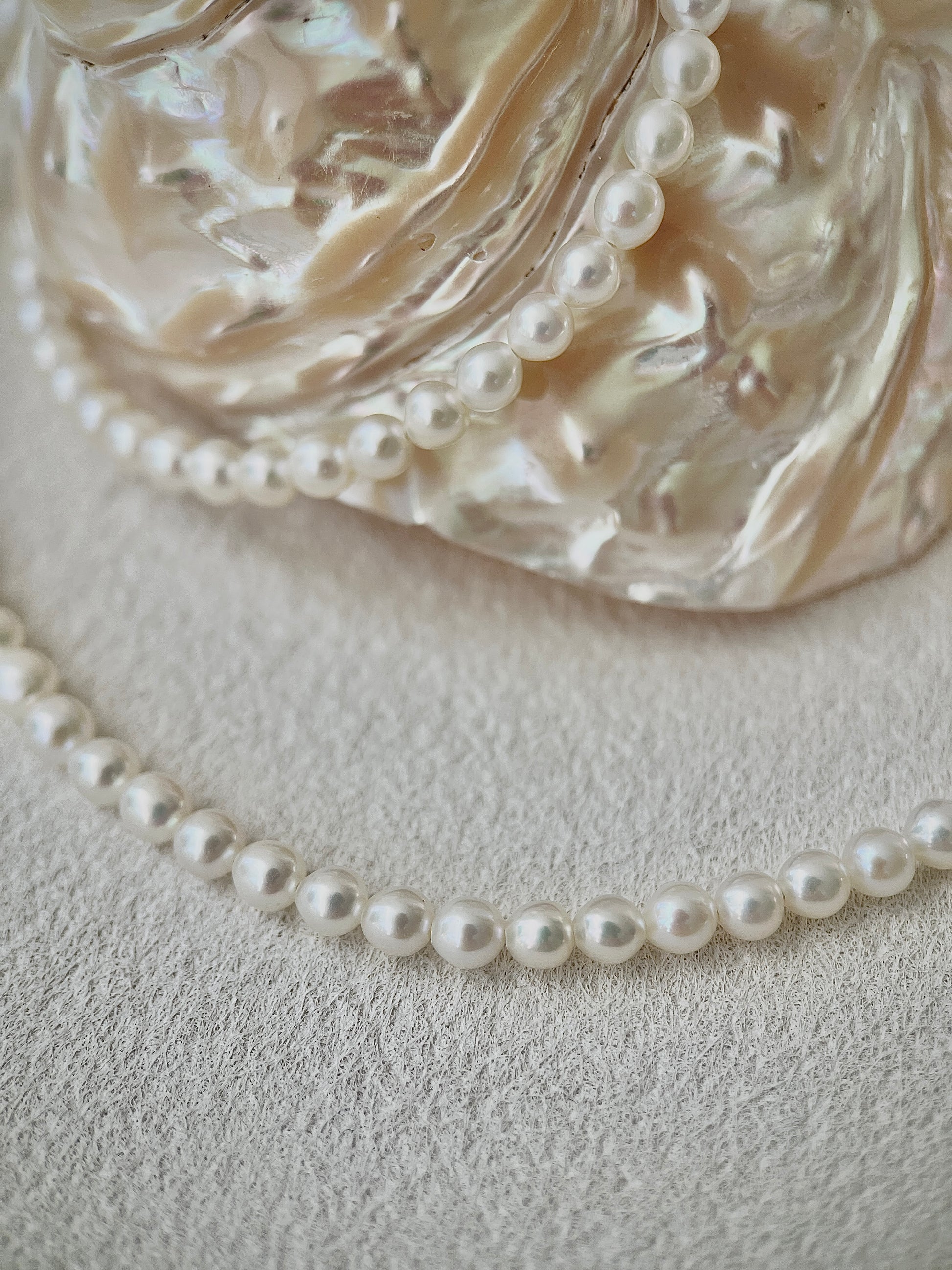 white Pearl necklace on a textured surface with a decorative glass bowl in the background