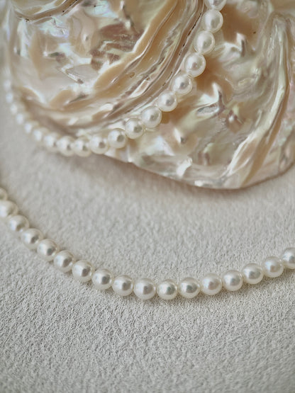 white Pearl necklace on a textured surface with a decorative glass bowl in the background