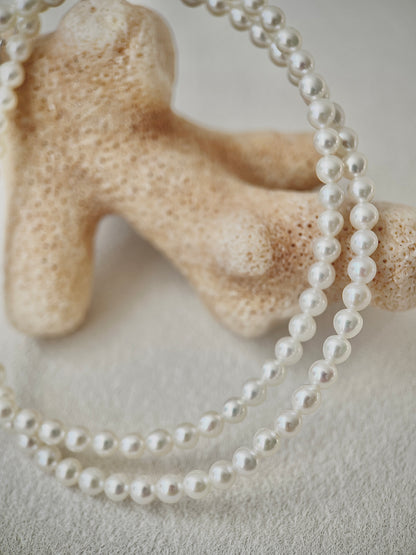 white Pearl necklace draped over a piece of coral on a neutral background