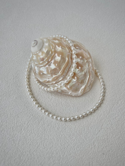 white Pearl necklace draped over an oyster shell on a light gray background