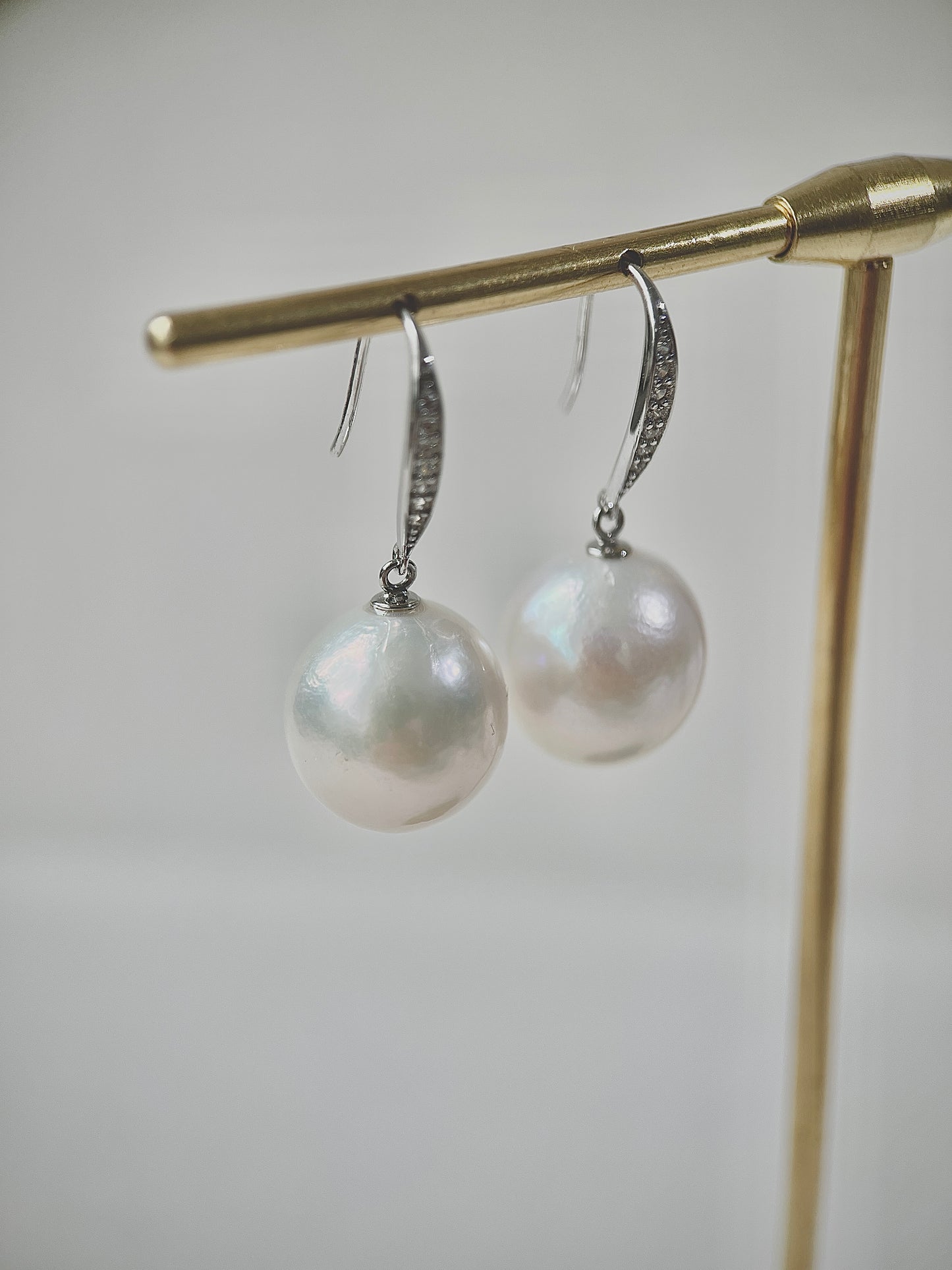 Pearl earrings hanging on a gold stand against a light background