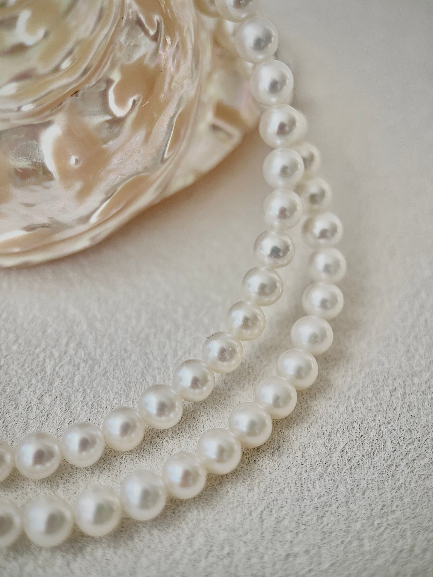 Pearl necklace on a textured surface with a decorative glass object.