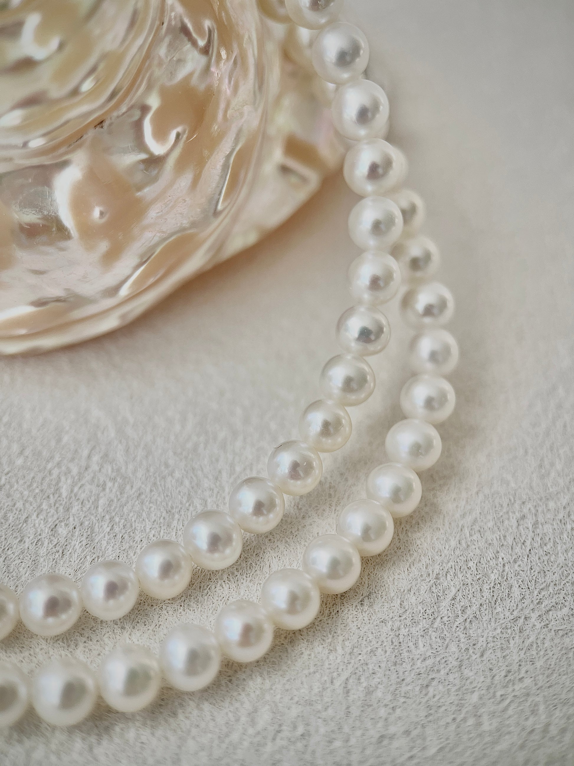 Pearl necklace on a textured surface with a decorative glass object.