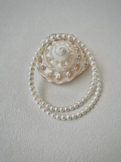 Pearl necklace draped over a shell on a light gray background