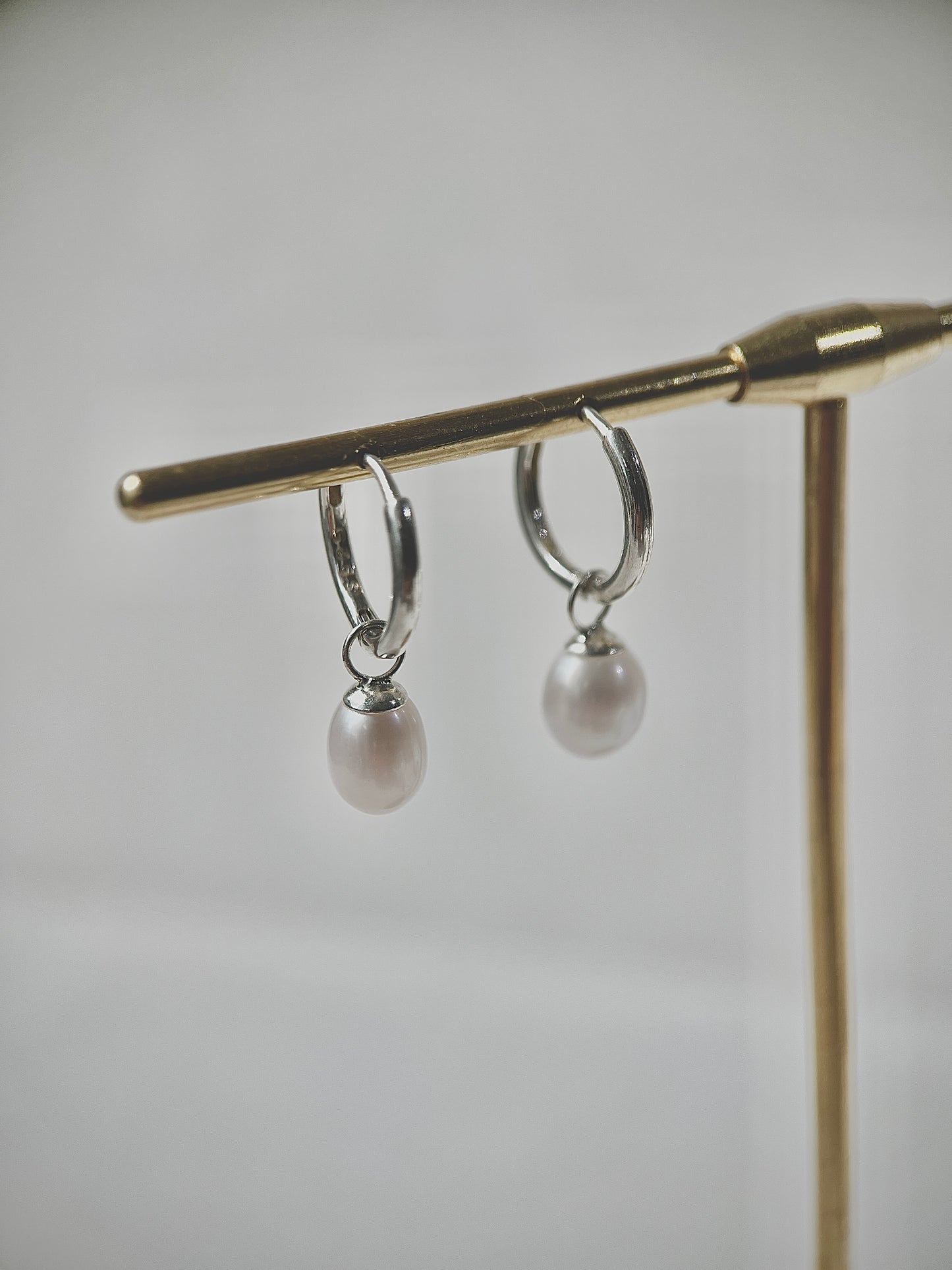 Silver hoop earrings with pearl drops on a gold stand against a gray background